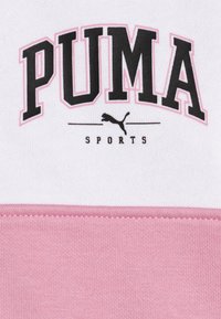 Vêtements de sport PUMA avec un schéma de couleurs blanc et rose, comportant de grosses lettres noires et un logo de puma. Matériel en coton doux, texture côtelée.