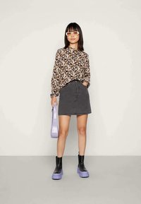 Blusa preta de flores com mangas longas, saia mini de denim cinza, botas confortáveis pretas com solas roxas e uma mala lavanda.