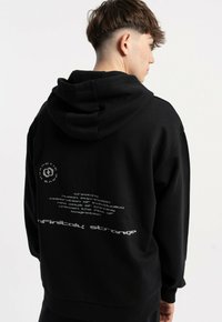 Czarna bluza z kapturem, z dużym kapturem i grafiką tekstową na plecach. Materiał wydaje się miękki, z luźnym krojem i ściągaczami przy mankietach.