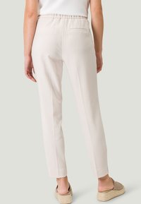 Pantalons tapered beige clair avec une ceinture élastique, deux poches arrière et une texture lisse, associés à des chaussures espadrilles tan.