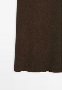 Tissu tricoté marron foncé avec une texture en côtes et une petite fente sur le côté à l'ourlet, arrière-plan blanc.