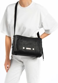 Zwarte leren schoudertas met een rechthoekige vorm, voorzien van een ritsluiting, decoratieve rhinestones en een verstelbare schouderband.