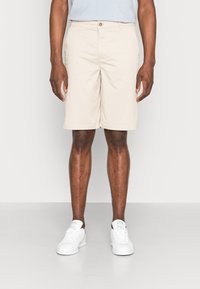 Beige shorts lavet af letvægtsstof, med knaplukning, sidelommer, og en lige pasform, parret med hvide sneakers.