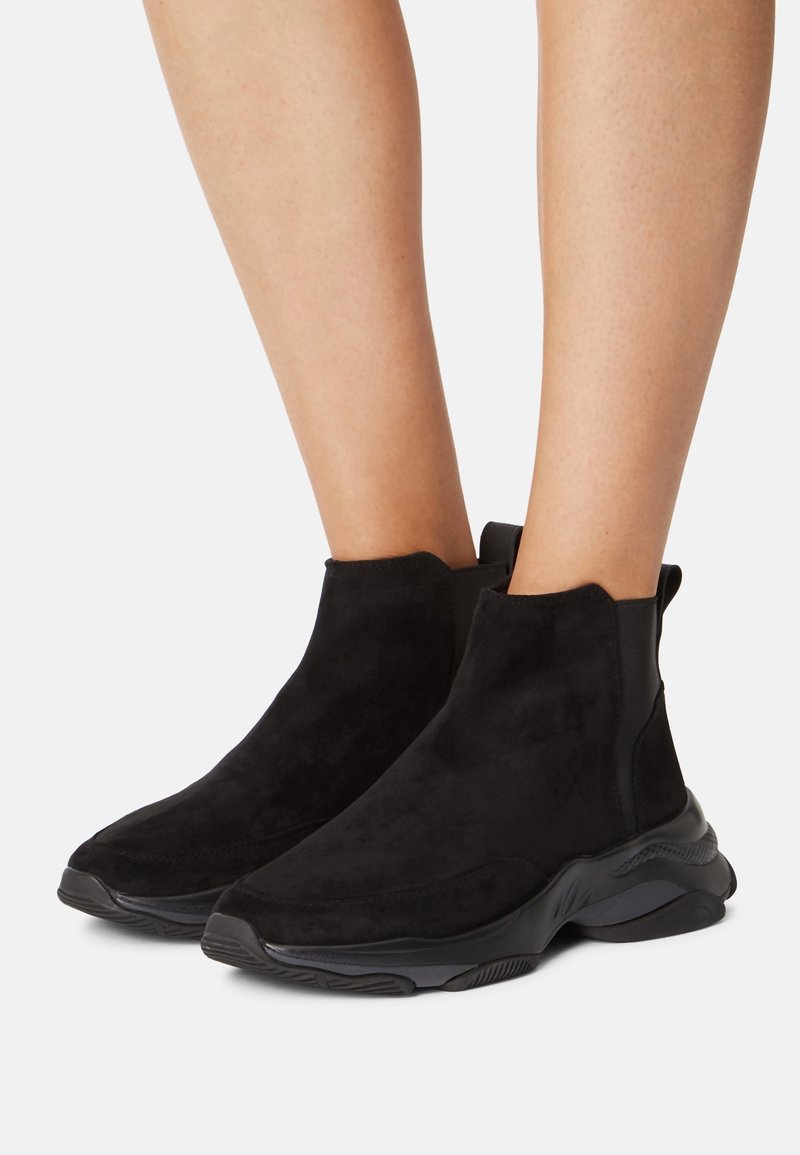Svarta mocka ankelskor med en slät yta, elastisk sidopanel och en kraftig svart sula. Kurvad design med minimal dekoration.
