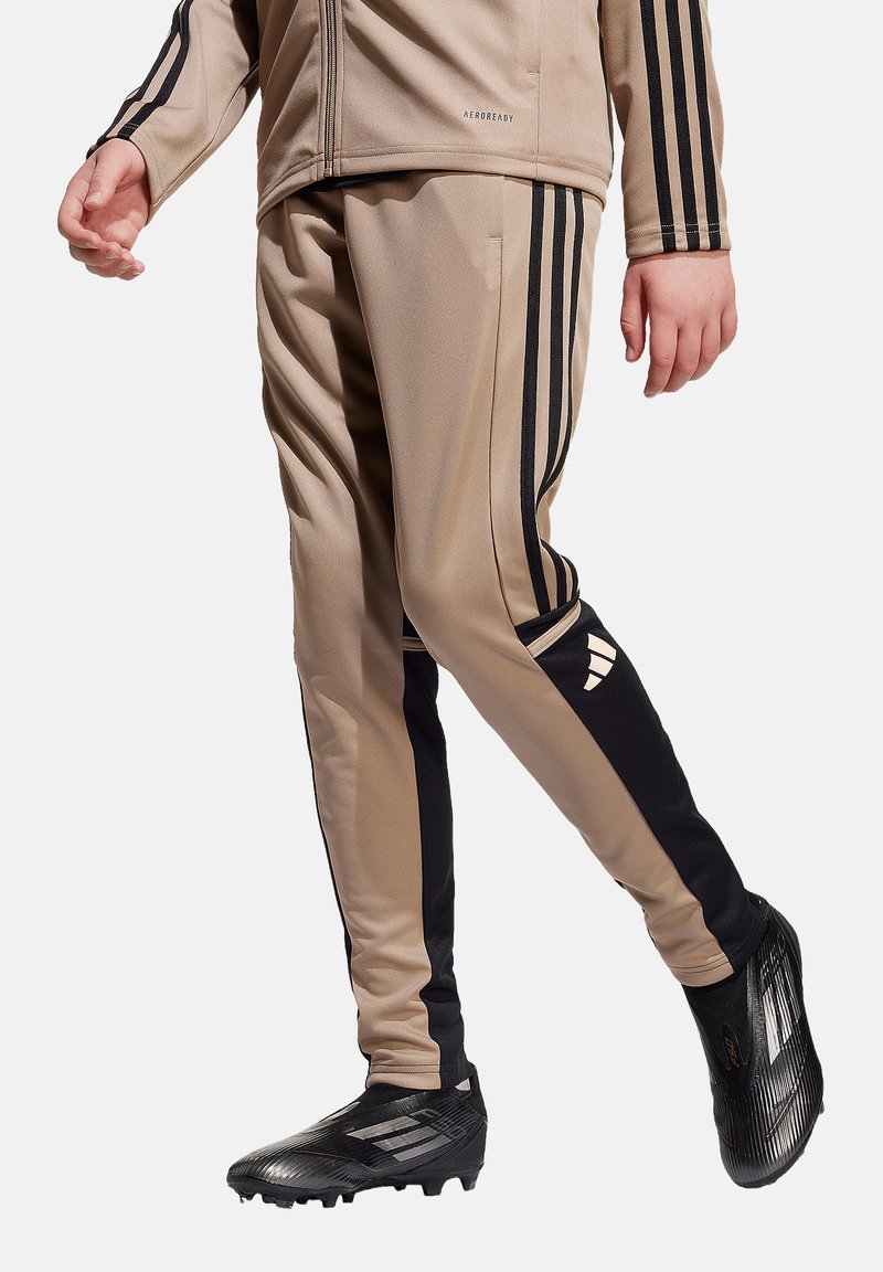 Beige Sporthosen mit schwarzen Seitenstreifen und einem Adidas-Logo, aus glattem Material, mit einem taillierten Schnitt und schmal zulaufenden Beinen.