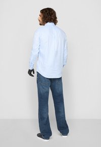 Lysblå ternet skjorte med lange ærmer indstoppet i mørkeblå denimjeans. Bagven, med knap-ned krave og buet kant.