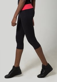 Leggings capri noirs avec une ceinture rose contrastante, au design ajusté et à la texture lisse, assortis à des baskets montantes noires.