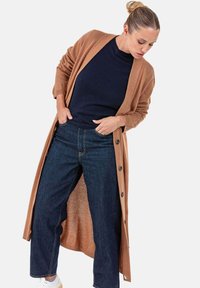 Langer, offen geschnittener Cardigan in camel-farbenem Strick, getragen über einem marineblauen Pullover und hoch taillierten dunklen Jeans. Verfügt über dezente Knöpfe und eine lässige Passform.