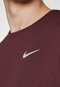Bordó Nike póló kerek nyakkal és rövid ujjal. Fehér kis Nike logó található a bal mellrészen. Simája anyag.