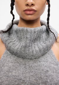 Top grigio lavorato a maglia con colletto alto a coste. Presenta un motivo di lavorazione testurizzato su tutta la superficie, design senza maniche con spalle scoperte.