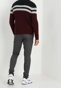 Pull en maille bordeaux avec des rayures noires et blanches sur les épaules, associé à un pantalon gris slim et des baskets blanches.