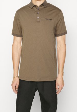 Braunes Poloshirt mit einem Kragen, vier Knöpfen und einem dezenten gestickten Logo. Gerippte Bündchen und gerader Saum. Glatte Textur.