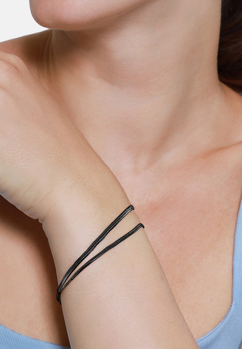 Bracciale intrecciato nero avvolge il polso più volte, caratterizzato da una texture liscia e un design sottile e flessibile.