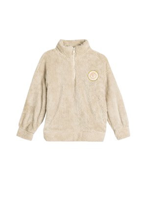 Pull en polaire beige avec une fermeture éclair quart de manière, manches longues, et un patch rond avec un cœur doré et blanc sur la poitrine.