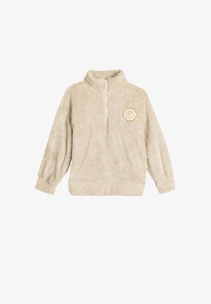 Beige fleece-paita, jossa on neljännesvetoketju, pitkät hihat ja pyöreä patch, jossa on kultainen ja valkoinen sydäntoteutus rinnassa.