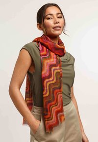 Écharpe multicolore avec des motifs ondulés dans des tons rouges, orange et violets ; tissu léger et transparent drapé autour du cou.