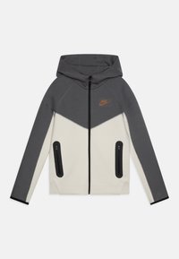 Grauer und cremefarbener Kapuzenpullover mit durchgehendem Reißverschluss, der ein dreieckiges Farbkombinationsdesign und zwei seitliche Reißverschlusstaschen aufweist. Nike-Logo in Orange.