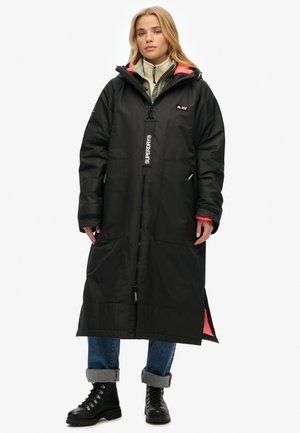 Manteau long noir en matériau résistant à l'eau, avec une fermeture éclair, deux poches pour les mains, et une touche de corail au col et à l'ourlet.