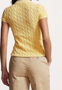 Gul stickad polo-tröja med en strukturerad kabeldesign, korta ärmar och ribbad krage, i kombination med beige byxor.