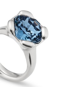 Une bague en argent dotée d'une grande pierre précieuse bleue facettée avec une forme angulaire distincte, sertie dans un bandeau lisse et poli.
