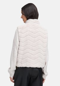 Kurze weiße Kunstfelljacke mit einem Zickzack-Textur, hohem Kragen und locker sitzenden Ärmeln, kombiniert mit schwarzen Hosen.