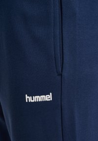 Granatowe dresy wykonane z miękkiego materiału, z białym logo "hummel" z boku oraz standardowym krojem i kieszeniami po bokach.