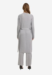 Grauer Strickcardigan mit geripptem Muster, tailliertem Design und langen Ärmeln, kombiniert mit passenden weit geschnittenen Hosen. Hohe Absätze runden das Outfit ab.