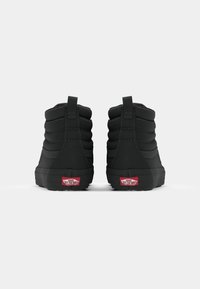 Black high-top shoes with padded sides, rubber soles, and red logo accents. Features stitch detailing and a pull tab at the back.
