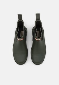 Bottes en caoutchouc vertes à hauteur de cheville avec des languettes, présentant une finition texturée et une doublure noire. Logo de la marque visible sur la semelle.