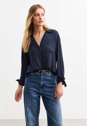 Navy button-up shirt with a collar, two chest pockets, and long sleeves, paired with high-waisted blue jeans. Smooth, textured fabric.
