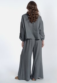 Set coordinato in lino grigio composto da un top corto a maniche lunghe e pantaloni a gamba larga. Il tessuto presenta un aspetto testurizzato e traspirante.