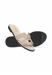 Beżowe sandały na płaskiej podeszwie z teksturowanymi syntetycznymi paskami, otwartym czubkiem i wyściełaną wkładką. Czarna gumowa podeszwa z subtelnym wzorem bieżnika.