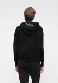 Μαύρη φούτερ μπλούζα με κουκούλα και ριμπ μανίκια και στρίφωμα, με λευκή επιγραφή "LeGer" στο πίσω μέρος. Λείο υλικό, άνετη εφαρμογή.