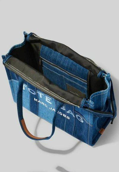 Borsa a spalla in denim con chiusura a zip, dettagli in pelle marrone e testo stampato bianco. Presenta una tasca interna e un ampio scomparto principale.