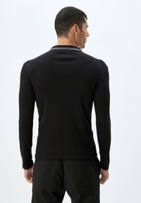 Svart långärmad polo med ribbad textur, med en kontrasterande randig krage. Enkelt design med en skräddarsydd passform.