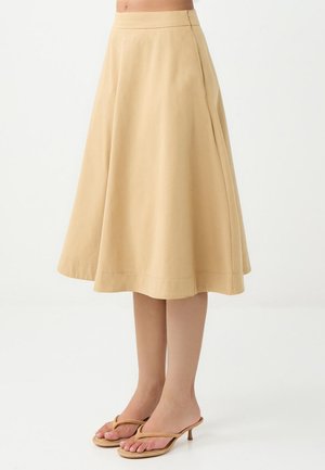 Jupe midi évasée beige en tissu doux, dotée d'une taille élastique et d'une fermeture éclair sur le côté. Associée à des tongs à talons couleur tan.