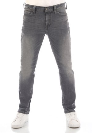 Jeans grigi slavati slim fit indossati da una persona con sneakers bianche, in piedi con le gambe leggermente divaricate su sfondo bianco.