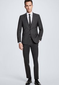 Kullsvart dress med slim fit, enknappet jakke, hvit skjorte og svart slips. Glatt stoff, minimal mønster, svarte sko.
