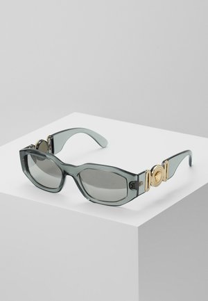 Occhiali da sole con tonalità grigia, montatura ottagonale, bracci trasparenti di colore grigio e finiture dorate, con un accento a medaglione sugli steli.