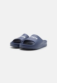 Sandales en caoutchouc bleu marine avec bout et talon ouverts. Présentent une semelle intérieure texturée et un logo "LACOSTE" blanc bien visible sur la sangle supérieure.