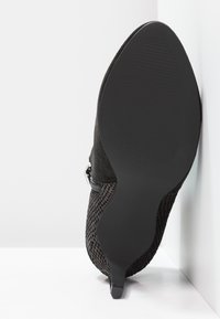 Zapato negro de tacón con parte superior de ante y detalles de malla. Tacón de aguja delgado y suela texturizada. Cierre de cremallera lateral.