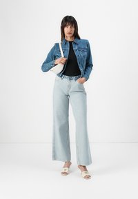 Denim jacket, black ribbed top, light blue wide-leg jeans, white handbag, and beige mules with logo detail. Simple, casual outfit.