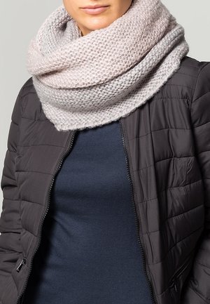 Personne portant une écharpe infinity en grosse maille gris clair, une veste matelassée foncée et un haut bleu marine, visible des épaules jusqu'à la bouche.