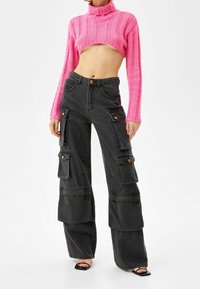 Rosa ribbad kort turtlenecktröja; högmidjade svarta cargobyxor med fickor och vikta fållar; modell som bär svarta blockklacksandaler.