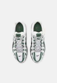 Paire de baskets Nike blanches et vertes avec des touches noires, des lacets détaillés et le logo "NIKE" sur la languette et la zone des orteils, vues de dessus.