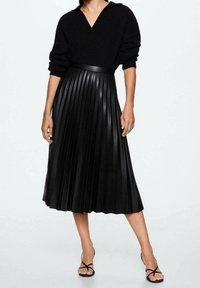 Jupe midi plissée noire fabriquée dans un matériau texturé, présentant une taille haute et un design fluide et élégant. Associée à un haut en tricot noir ample.
