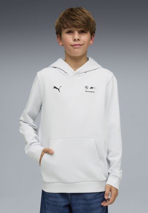 Dreng iført hvid BMW Motorsport-hættetrøje med Puma-logo, stående med den ene hånd i lommen mod en grå baggrund.