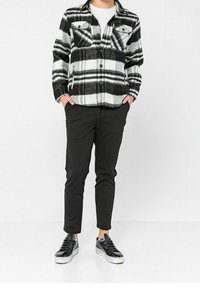 Svart- och vitrutigt flanellskjorta, knäppt, med två bröstfickor; kombineras med slim fit svarta byxor och glänsande svarta sneakers.