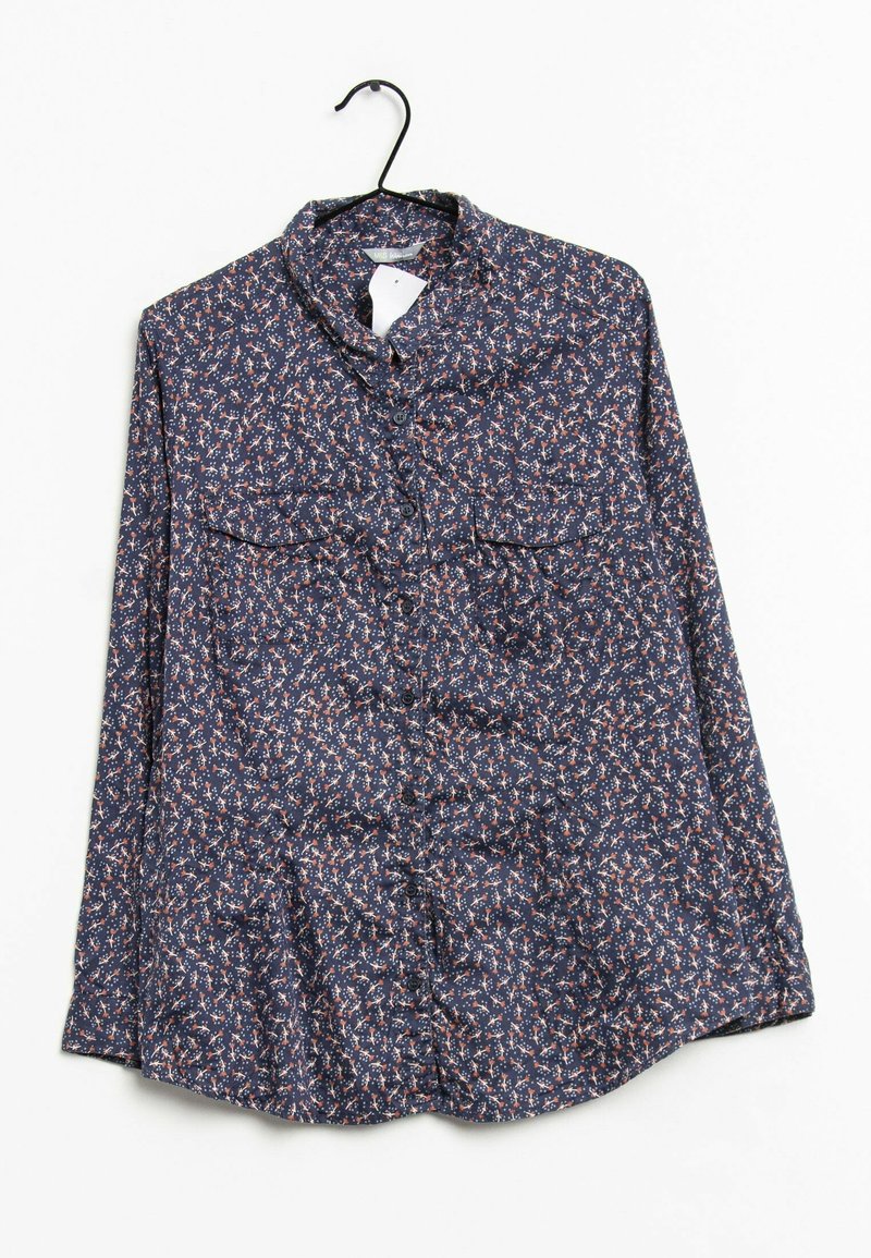 Chemise à manches longues boutonnée avec un petit motif floral multicolore suspendue sur un cintre noir sur fond blanc.