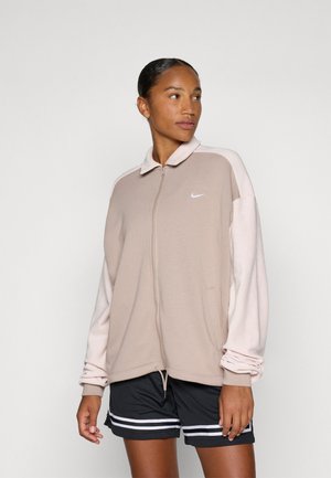 Beige Nike jakke med glidelås og lyserøde ermer, med krage, sidelommer og en liten hvit logo på brystet.
